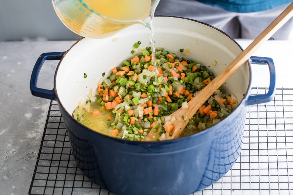 Adding chicken broth to a pot with mirepoix.