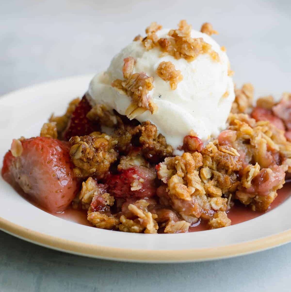 A bowl of strawberry crisp with vanilla ice cream on top.