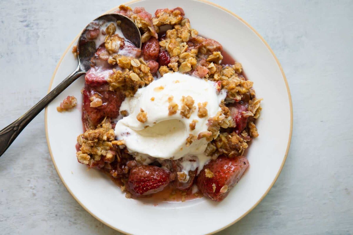 A bowl of strawberry crisp with vanilla ice cream on top.