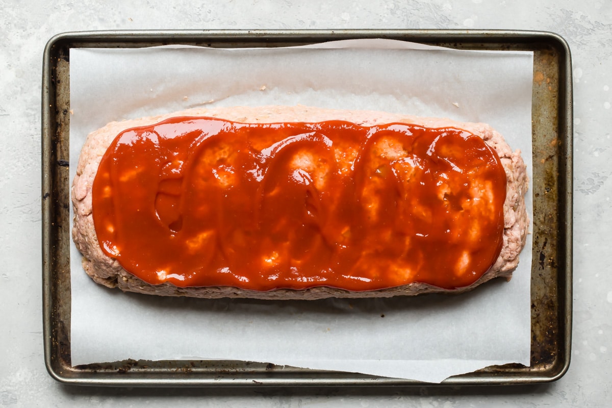 An unbaked turkey meatloaf with ketchup on top.