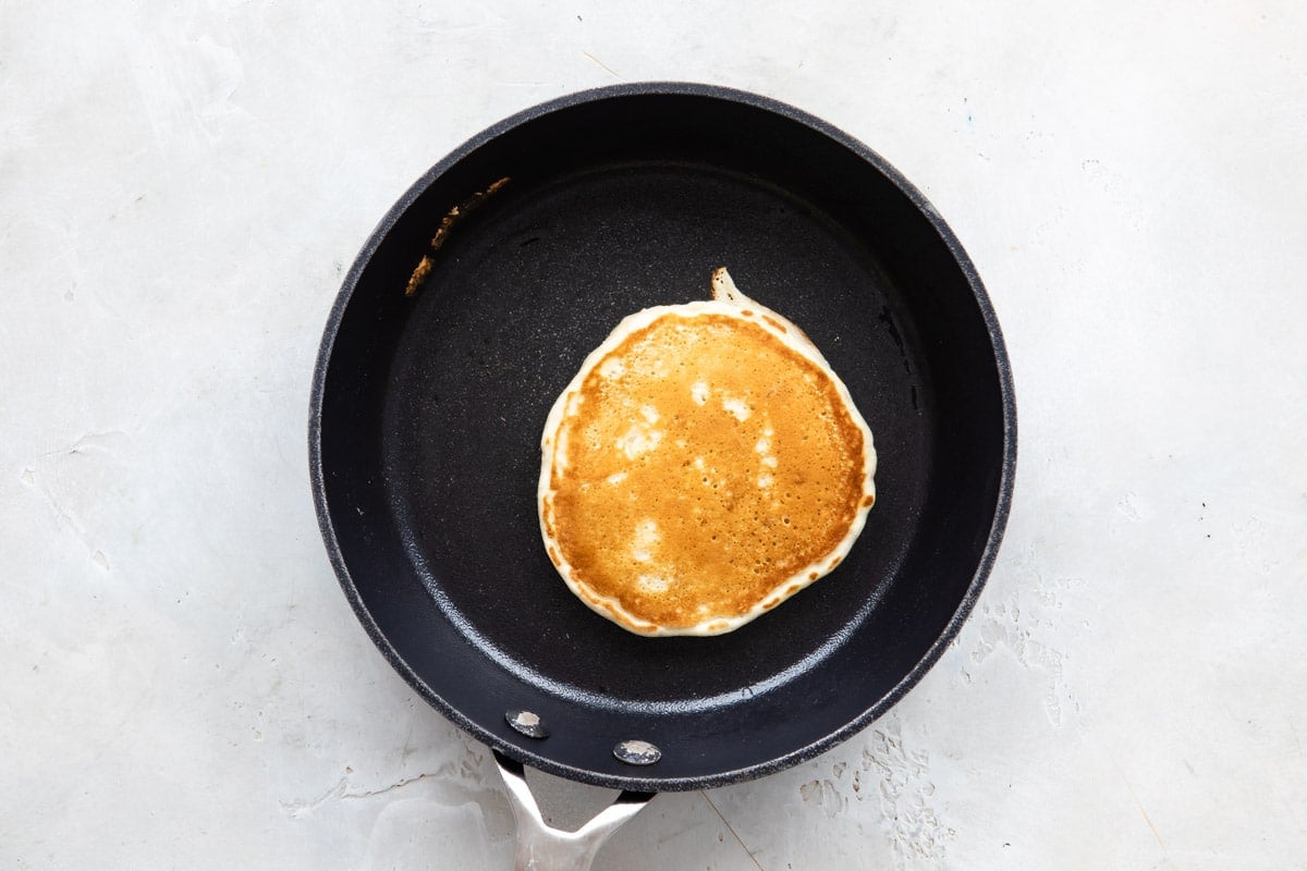 A Pancake in a skillet after flipping so cooked side is up.