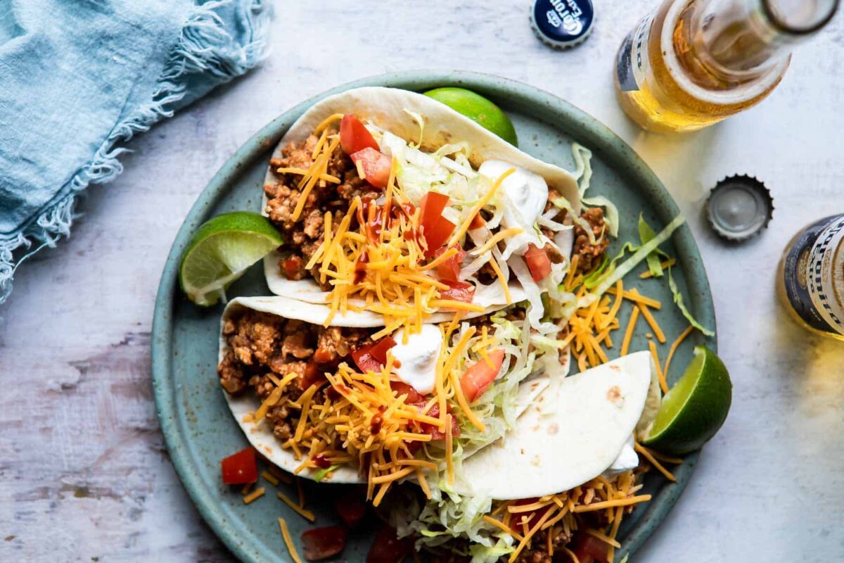 A platter of ground chicken tacos with cheese, sour cream, and tomatoes.