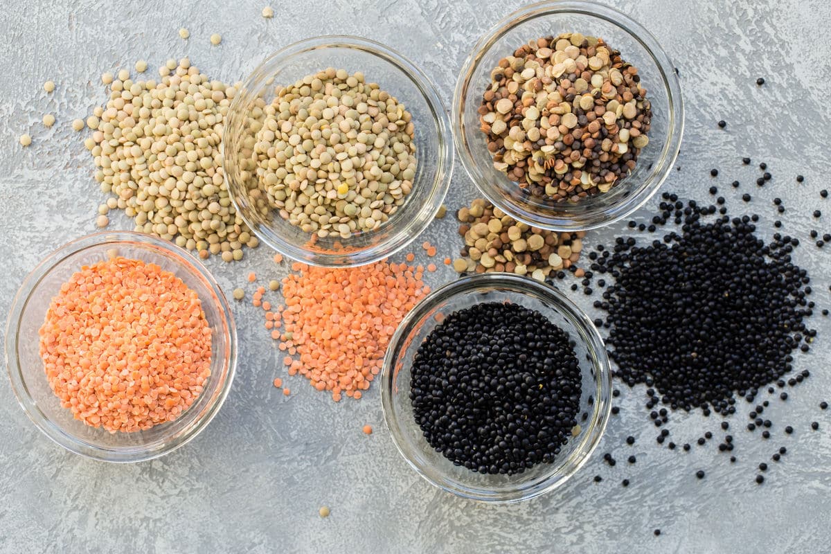 4 different types of lentils displayed in bowls with some of each spilled on to the table.