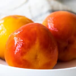 Three blanched peaches in a bowl.
