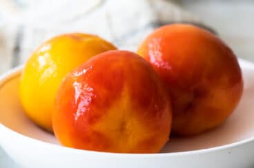 Three blanched peaches in a bowl.