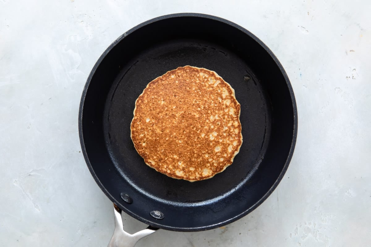 A Pancake in a skillet after flipping so cooked side is up.