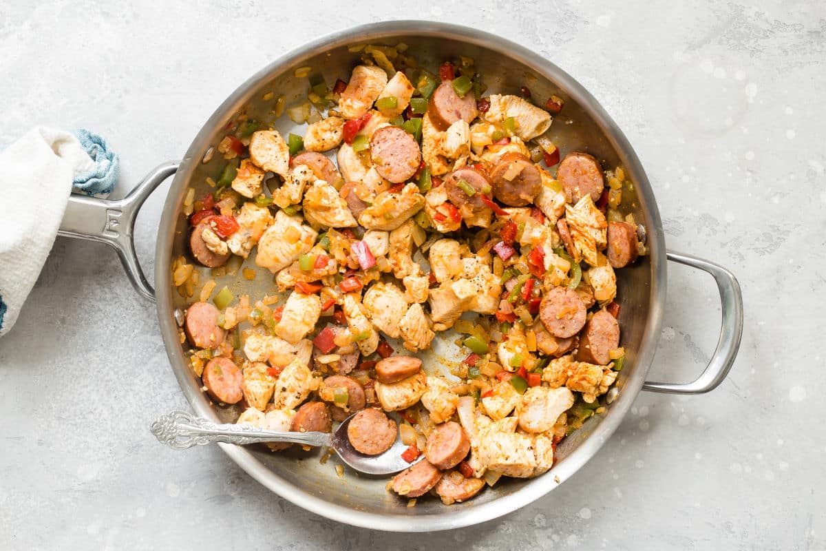 Sausage, chicken, and vegetables cooking in a skillet for Cajun pasta.