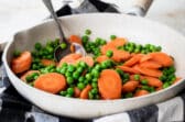Peas and carrots in a white frying pan.