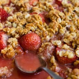 A baking dish of strawberry crisp with a spoon resting in it.