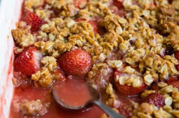 A baking dish of strawberry crisp with a spoon resting in it.