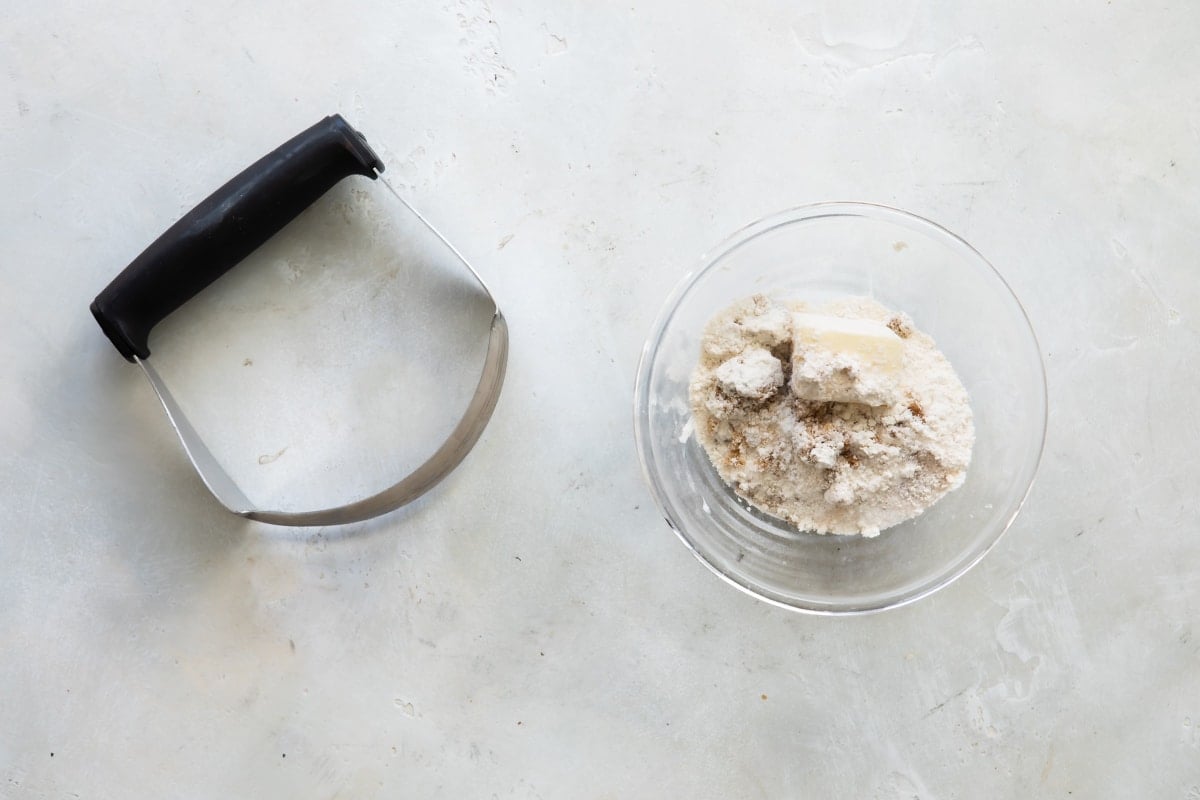 A pastry cutter next to a bowl of ingredients for streusel topping.