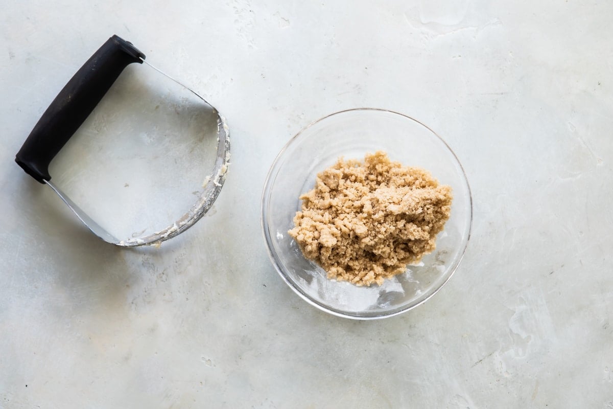 A pastry cutter next to a bowl of streusel topping.