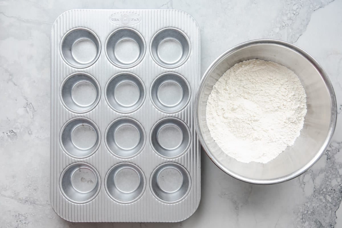 A muffin pan next to a bowl of flour, baking powder, and salt.