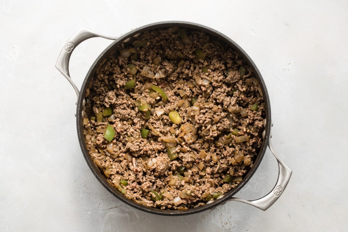 Browning ground beef with vegetables and chili spices in a skillet.