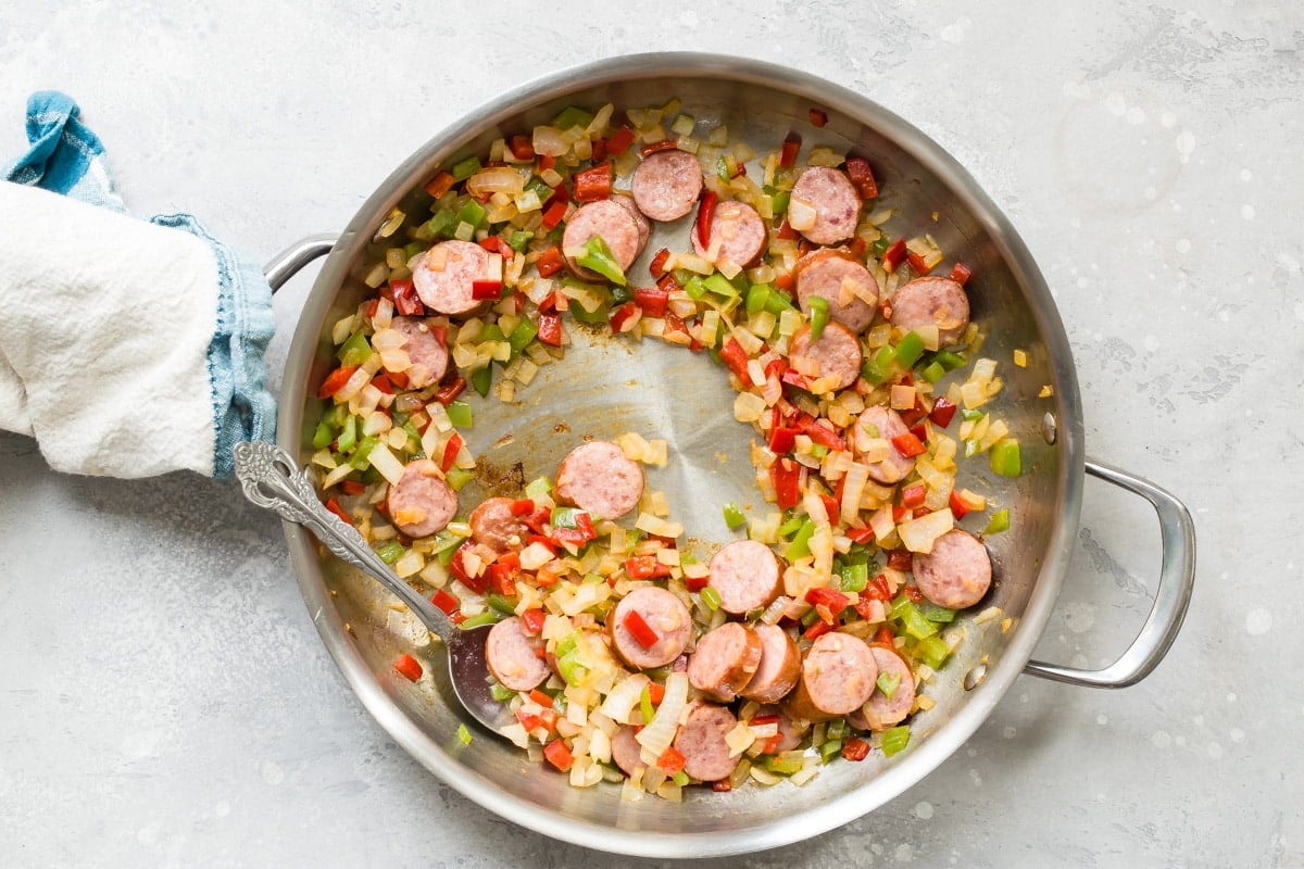 Sausage and vegetables cooking in a skillet for Cajun pasta.