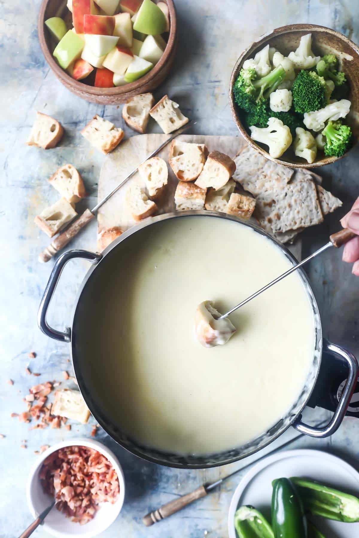 A pot of cheese fondue surrounded by bread and vegetables for dipping.