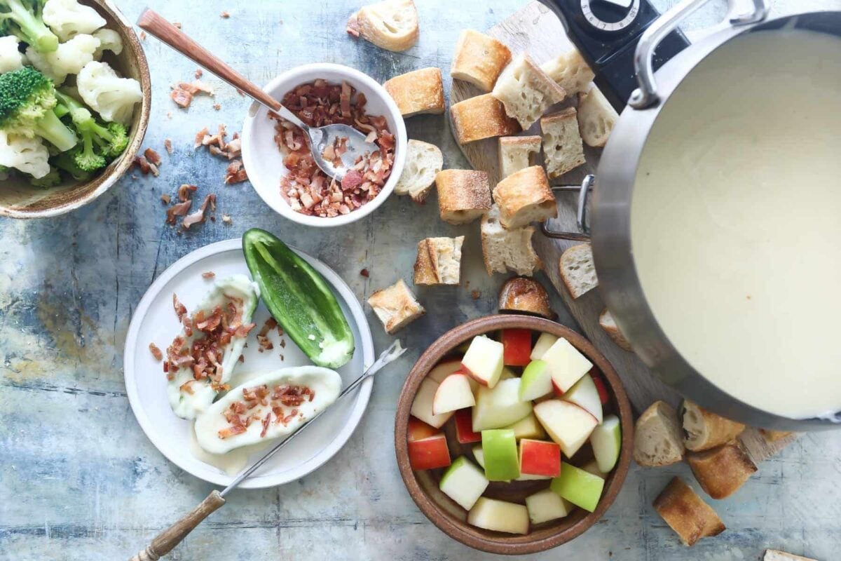 A pot of cheese fondue surrounded by bread and vegetables for dipping.