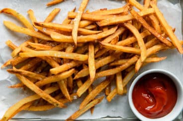 Homemade french fries on parchment paper next to a small cup of ketchup.