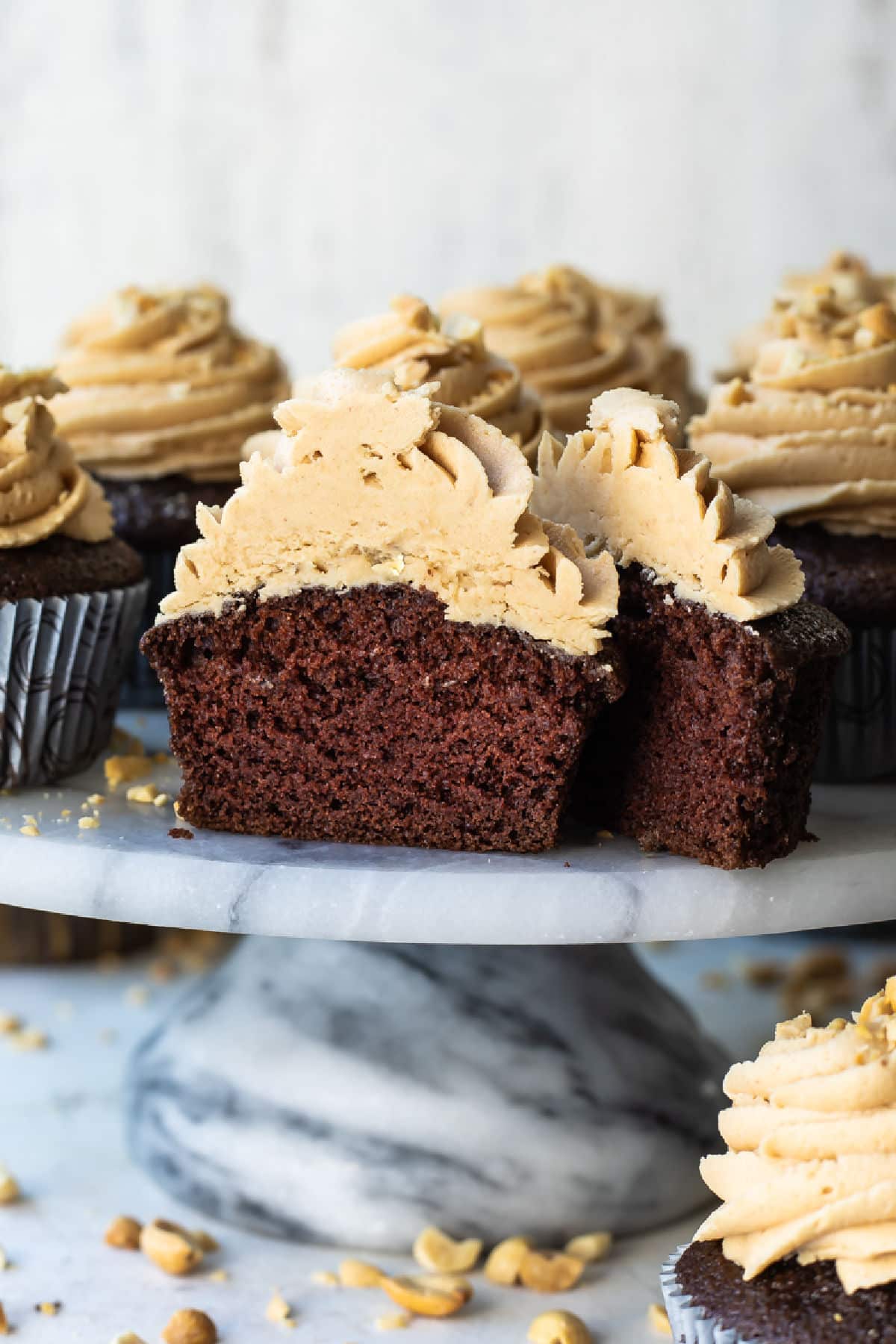 A cake stand filled with chocolate cupcakes with peanut butter frosting, 1 cut open to show the inside.