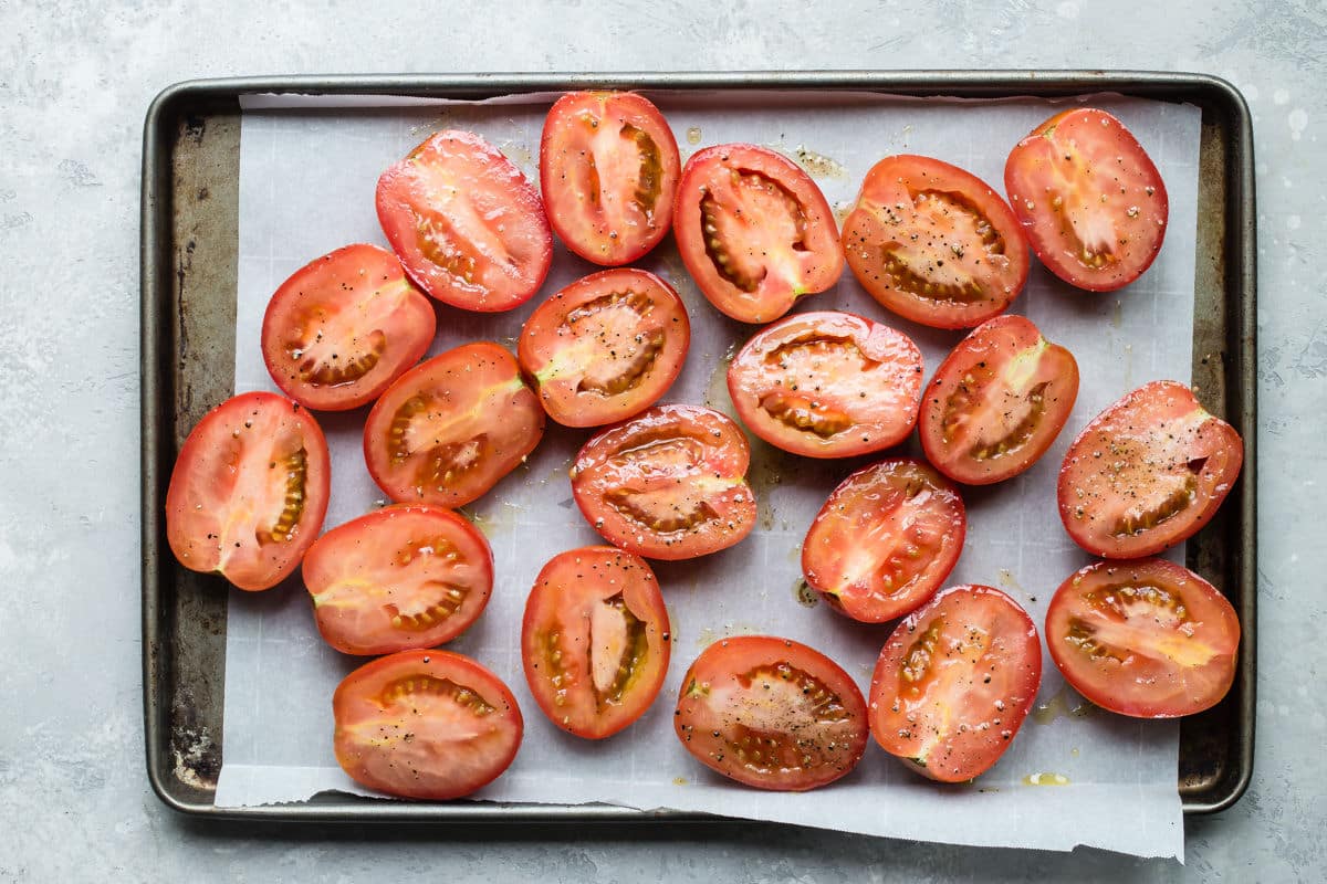 Raw tomatoes on a baking sheet to be roasted.