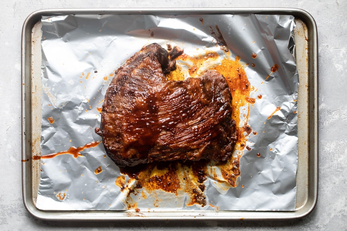A cooked slow cooker beef brisket on a metal foil lined pan.