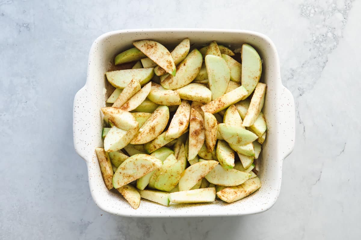 Sliced apples added to a baking dish to make apple cobbler.
