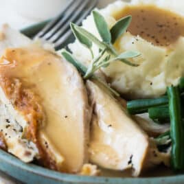 A plate of roast chicken with mashed potatoes, gravy, and green beans.
