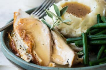 A plate of roast chicken with mashed potatoes, gravy, and green beans.