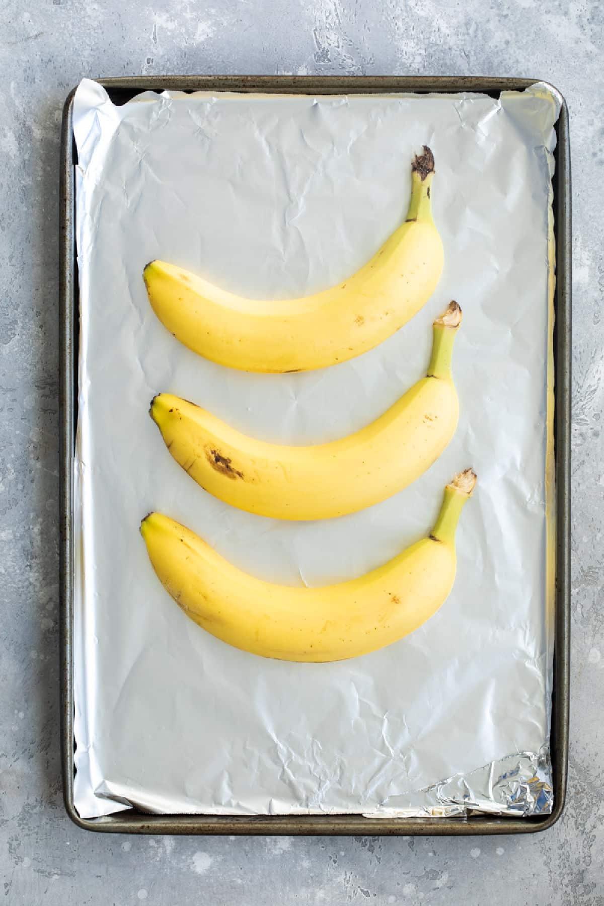 3 yellow bananas on a baking sheet.
