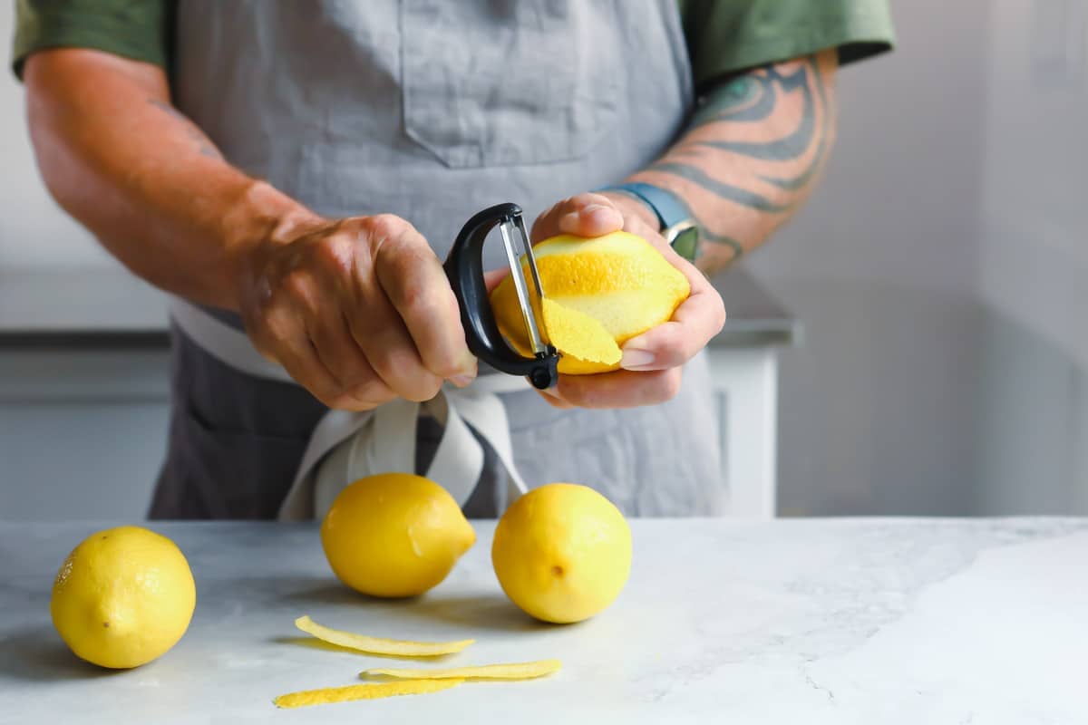 A lemon being zested with a peeler.