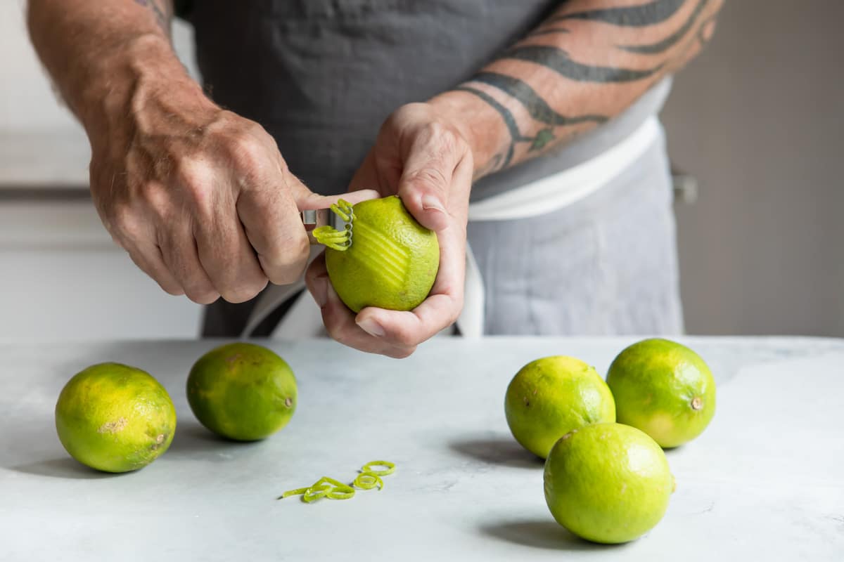Someone zesting a lime with a zesting tool.