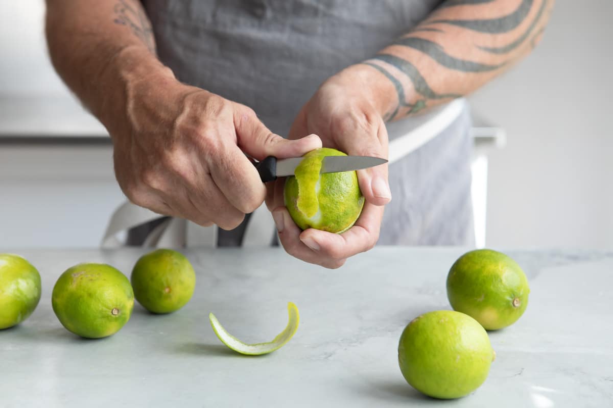 Someone peeling a lime with a paring knife.