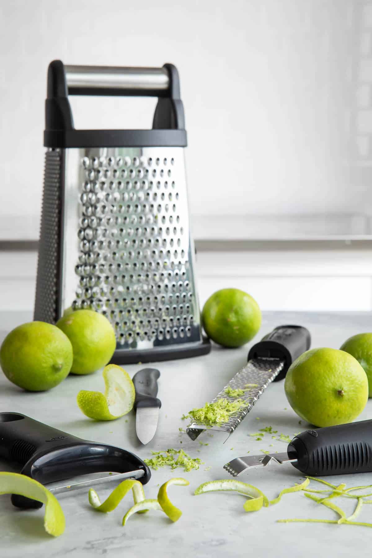 Zested limes and tools to zest a lime on a countertop.