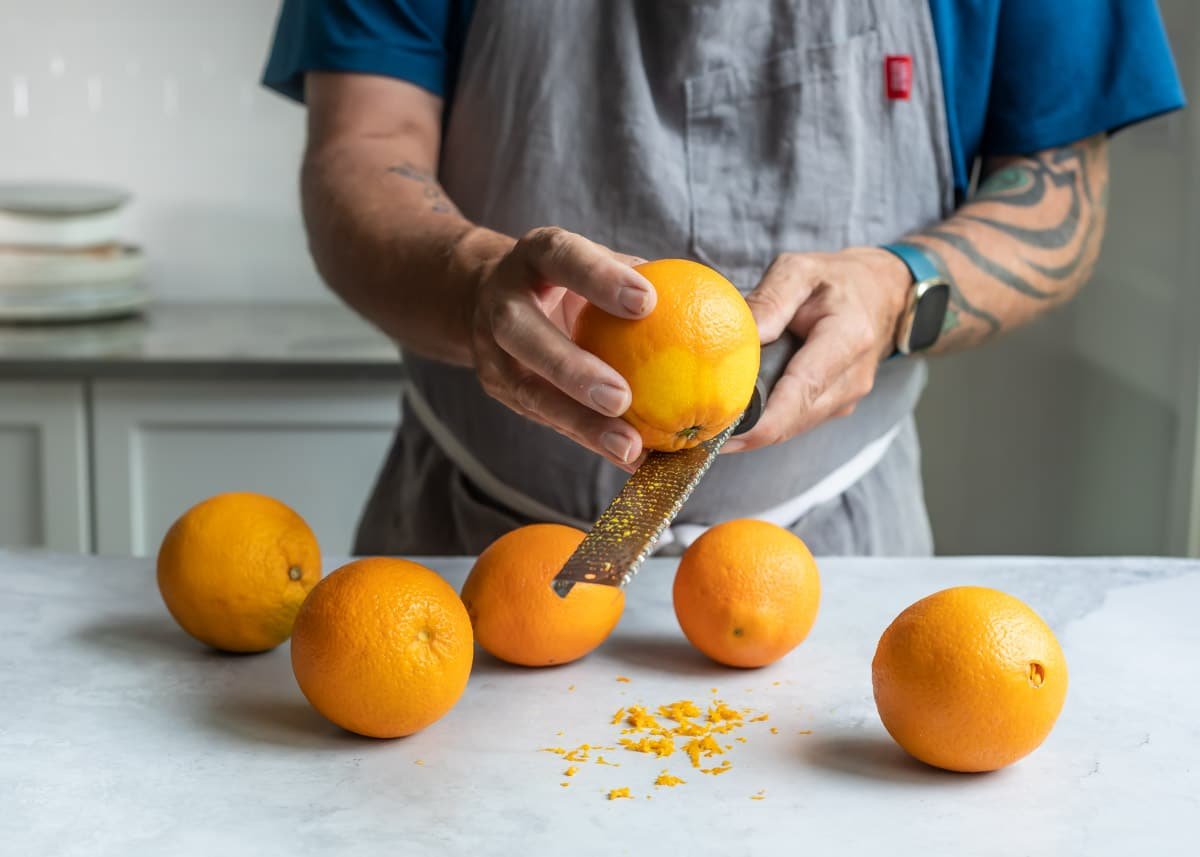 Someone zesting an orange with a microplane grater.