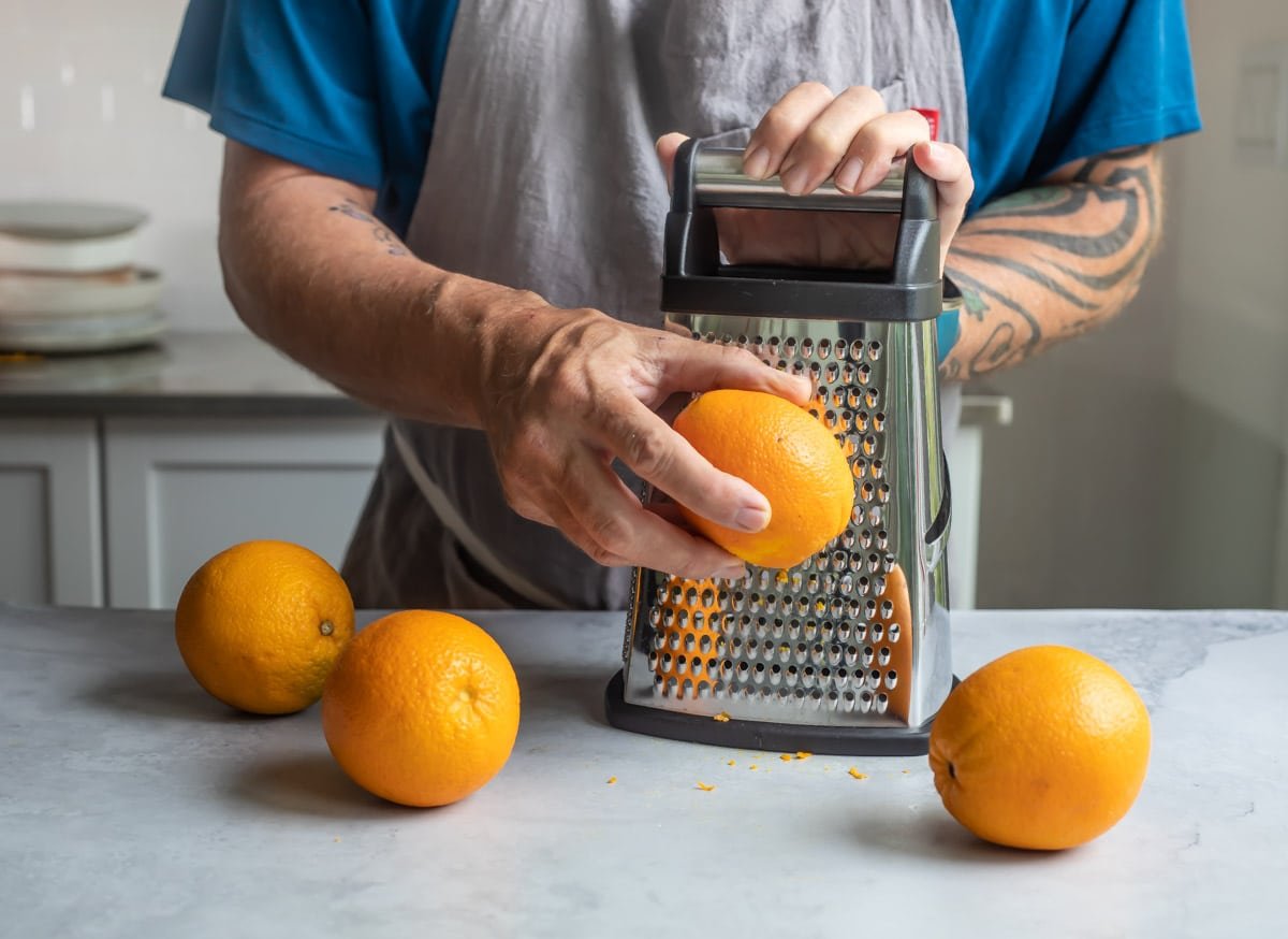 Someone zesting an orange with a box grater.