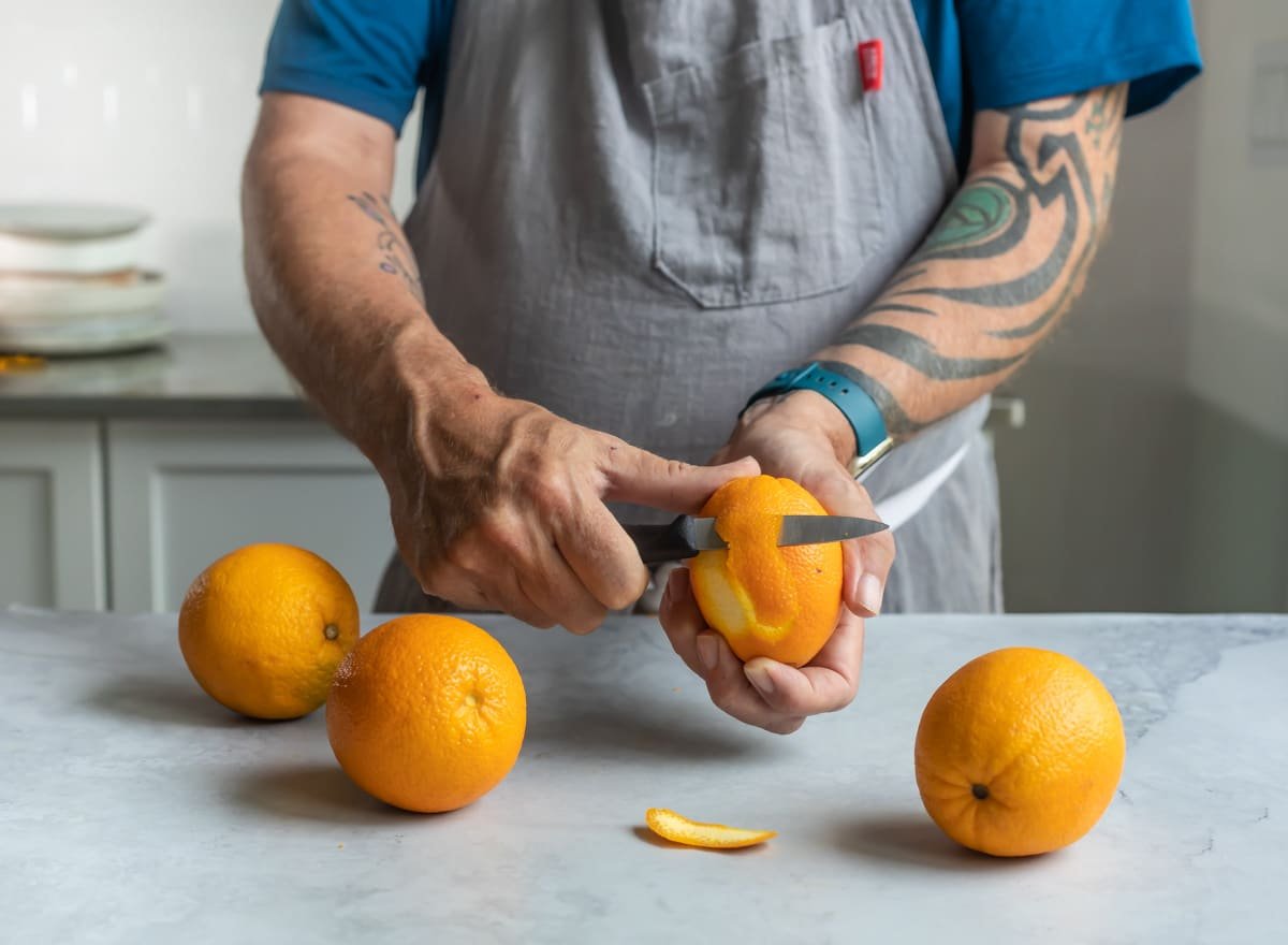 Someone peeling an orange with a paring knife.