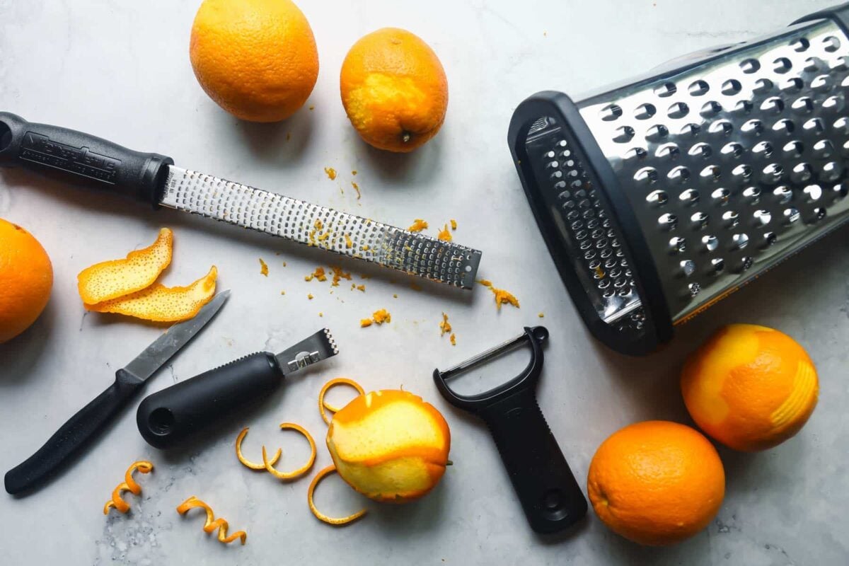 Five oranges on a countertop that have been zested with various tools.