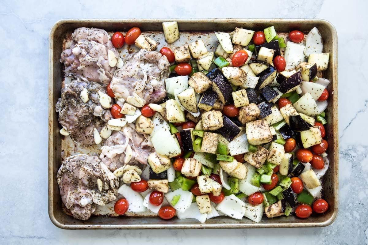 Italian-seasoned chicken with veggies on a sheet pan, uncooked.