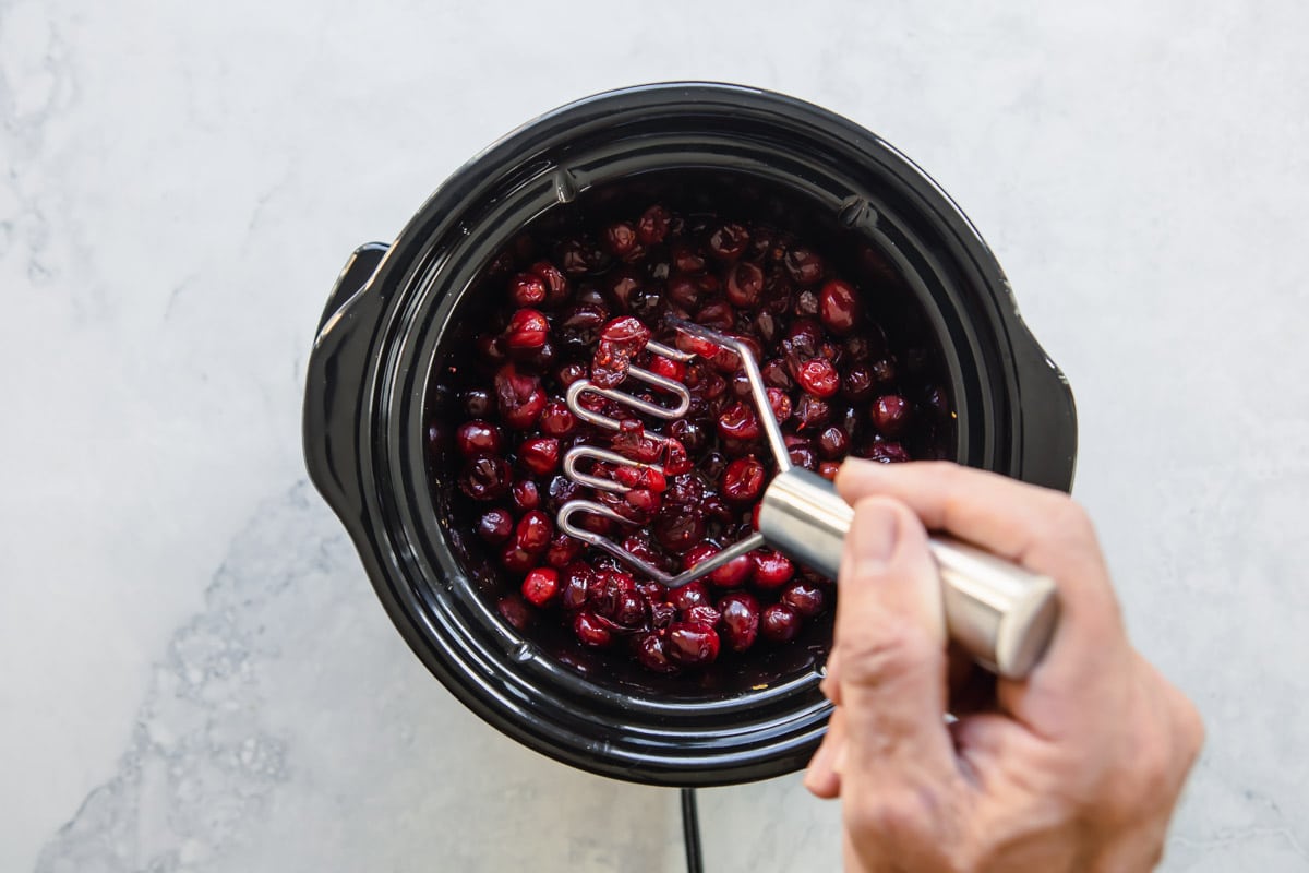 Mashing cranberry sauce in a slow cooker.