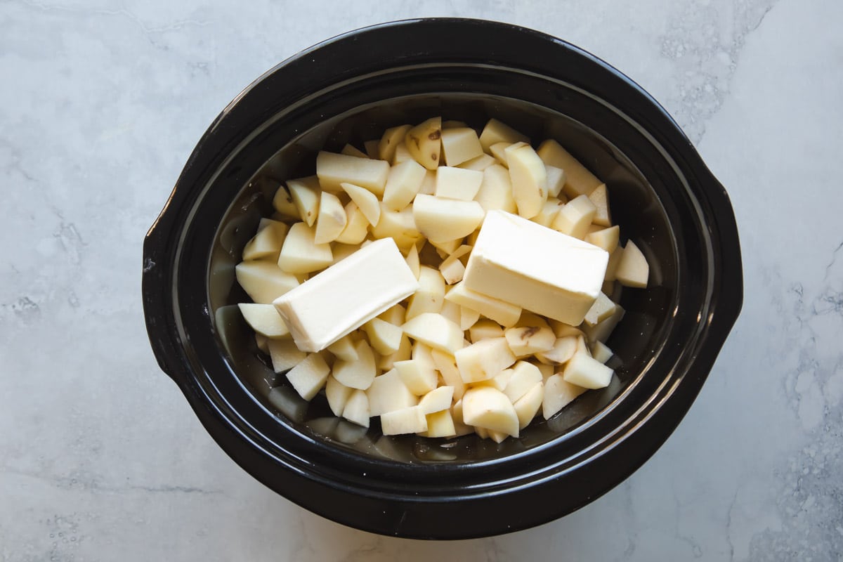 A crockpot full of diced potatoes cooking in milk and butter.