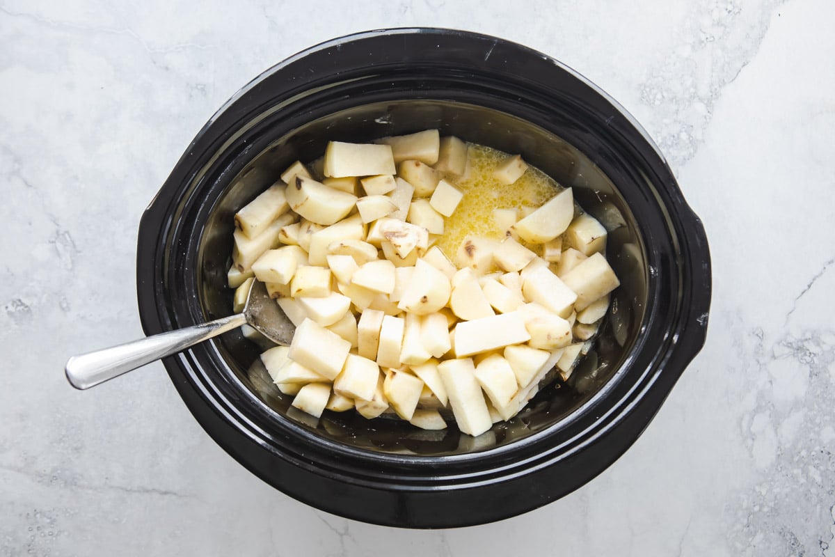 A crockpot full of diced potatoes cooking in milk and butter.