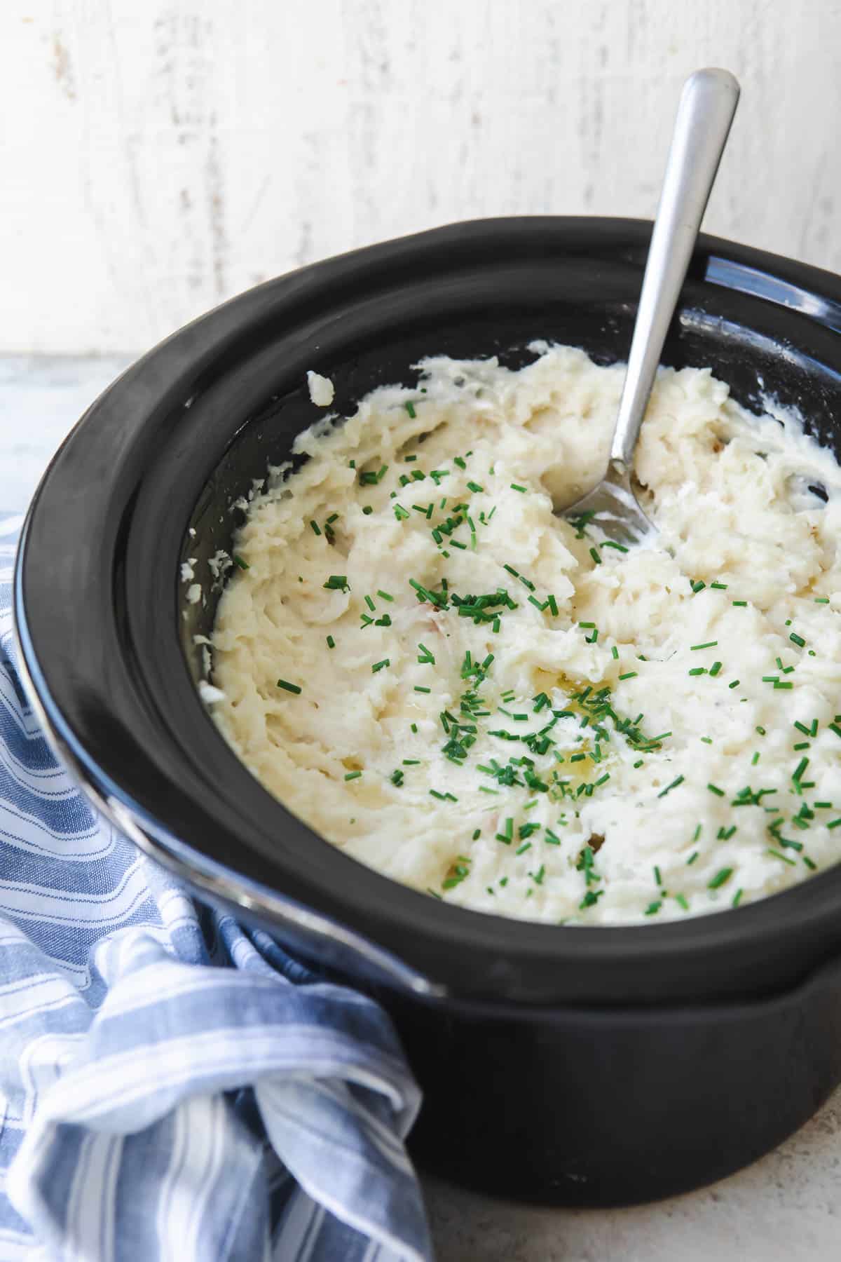 A crockpot full of mashed potatoes with chives on top.