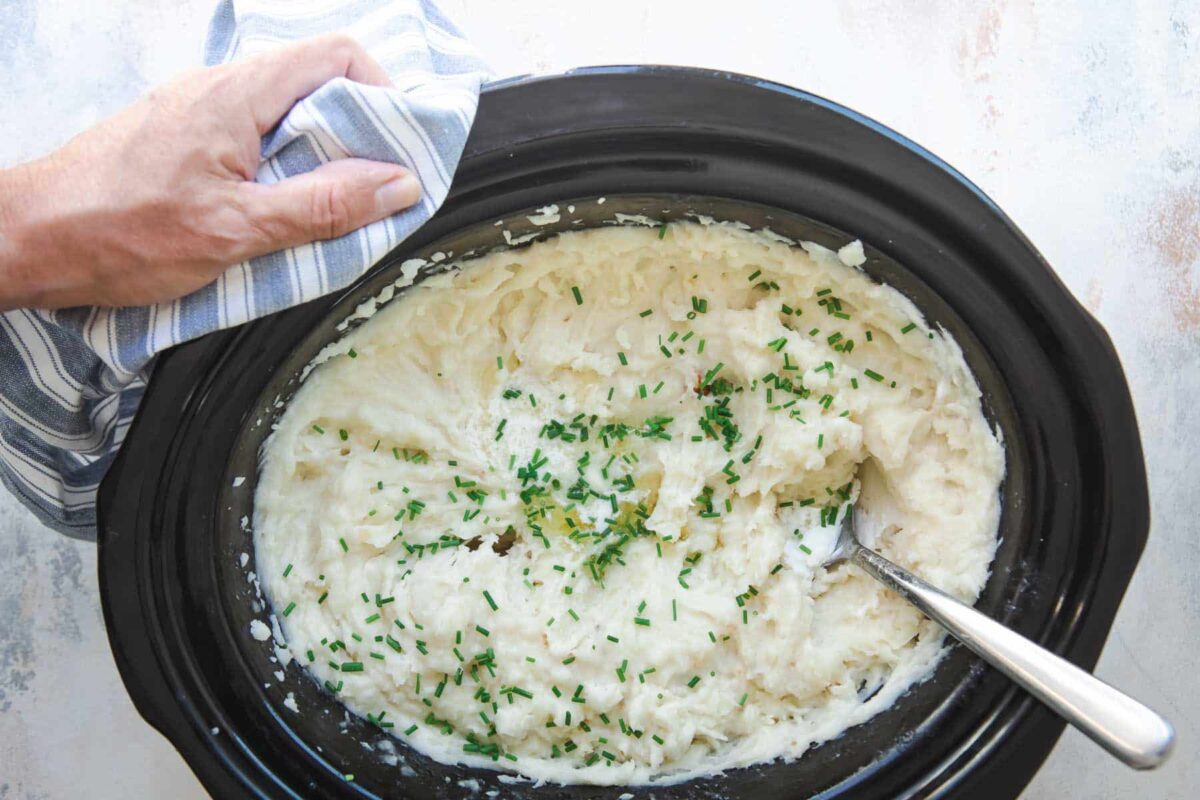 A crockpot full of mashed potatoes with chives on top.