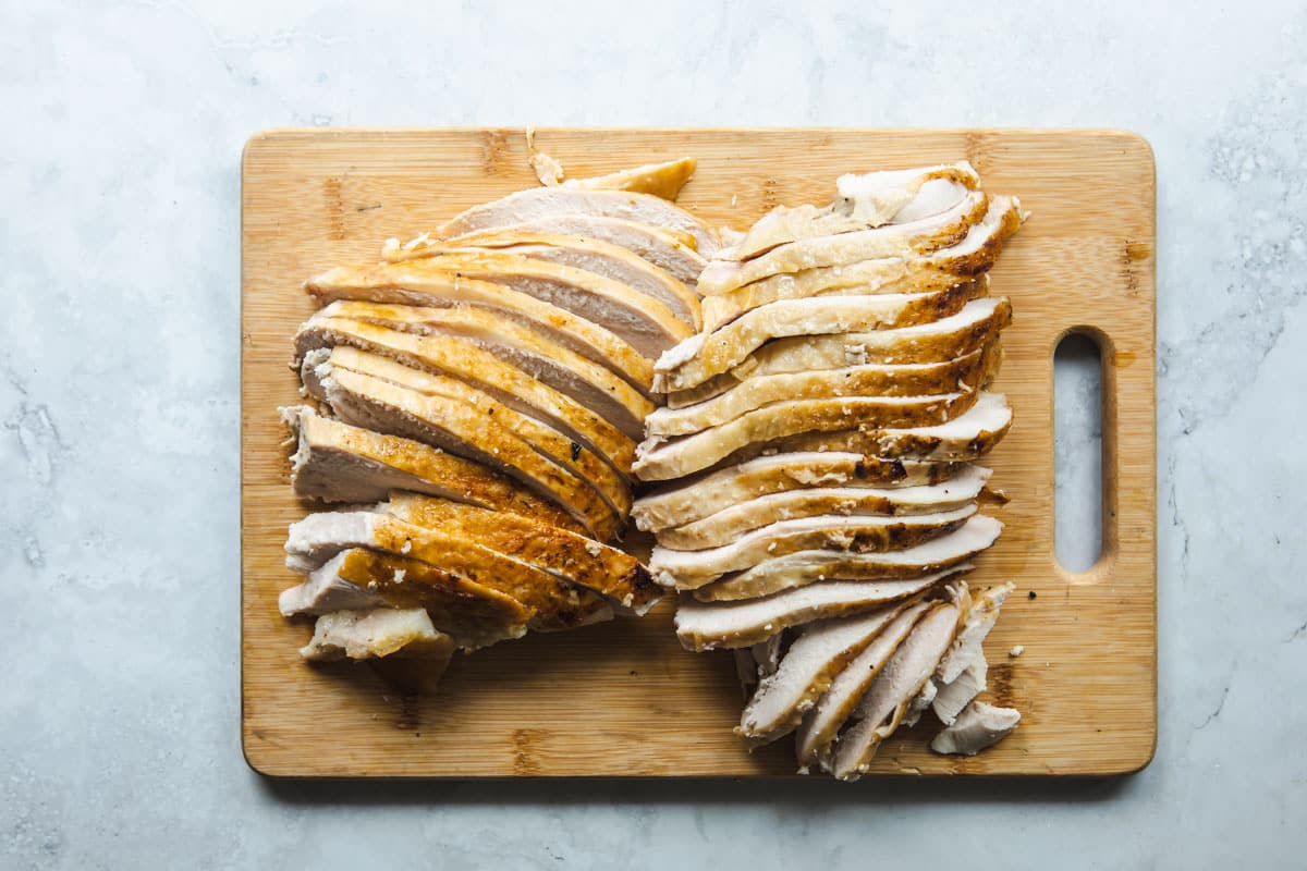 Slow cooker turkey breast slices on a wooden cutting board.
