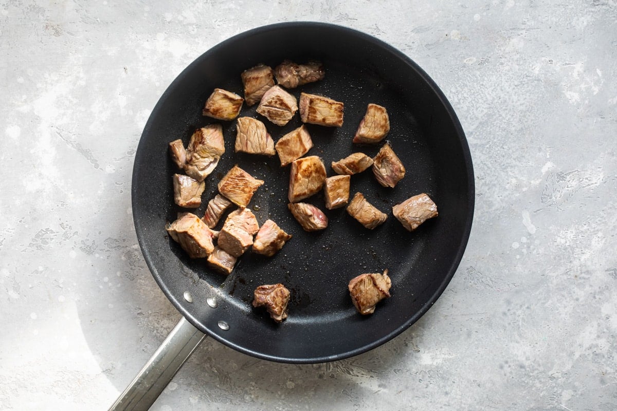 Steak tips cooking in a black skillet.