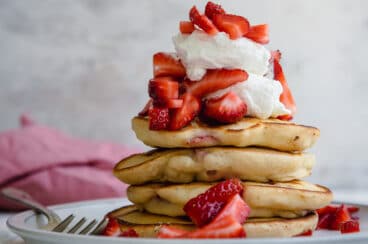 A stack of strawberry pancakes topped with whipped cream strawberries.