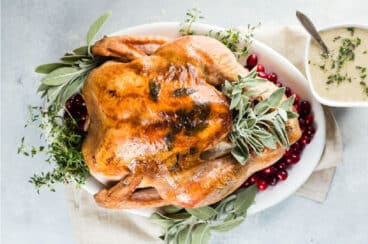 A roasted turkey on a platter with fresh herbs and cranberries.