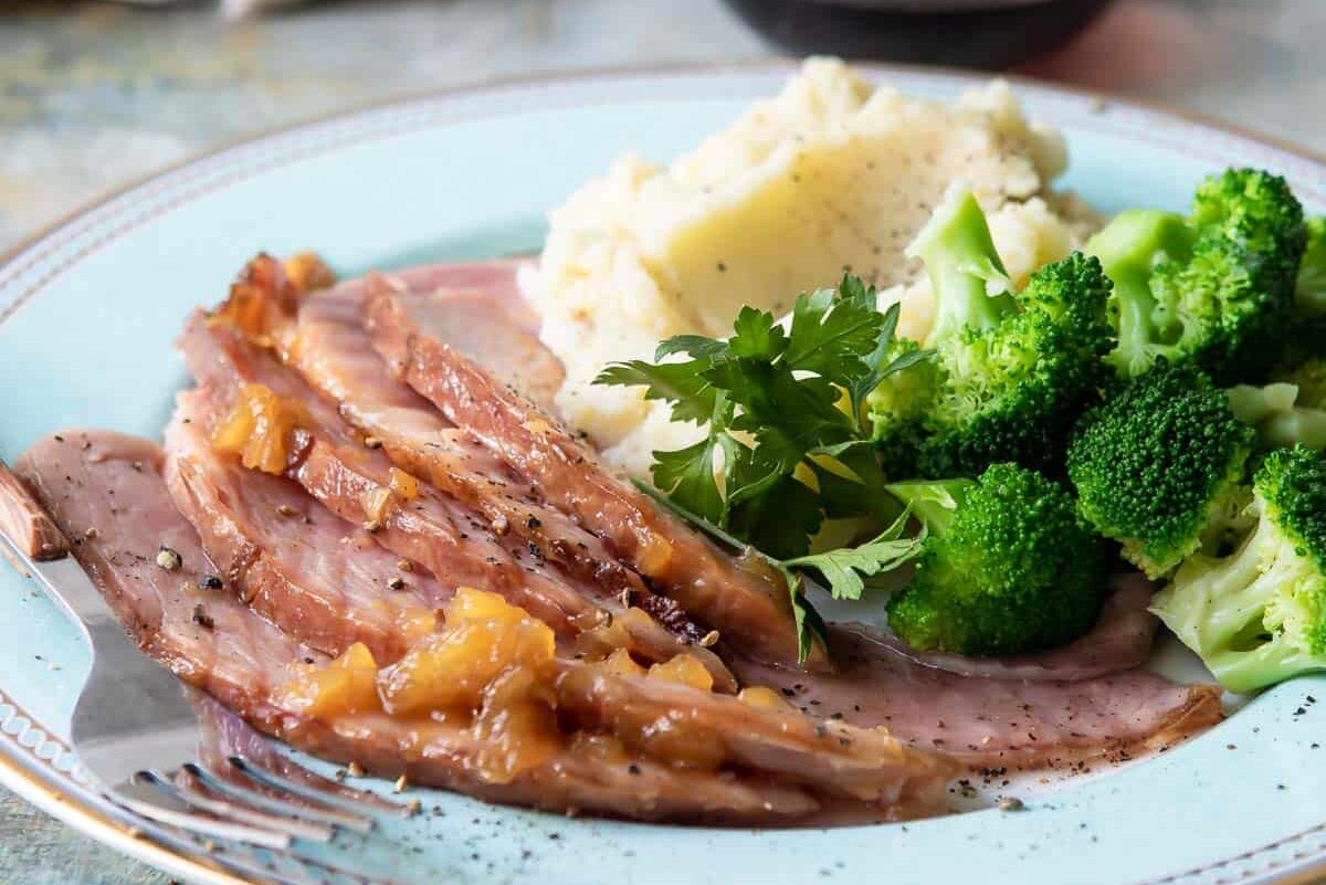 A plate of glazed ham, mashed potatoes, and broccoli.