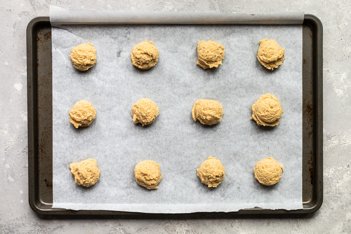 Twelve balls of peanut butter cookie dough on a baking sheet lined with parchment paper.