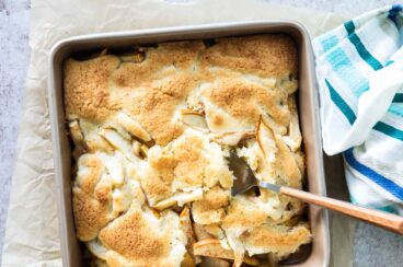 A pear cobbler in a square pan with a spoon resting in it.